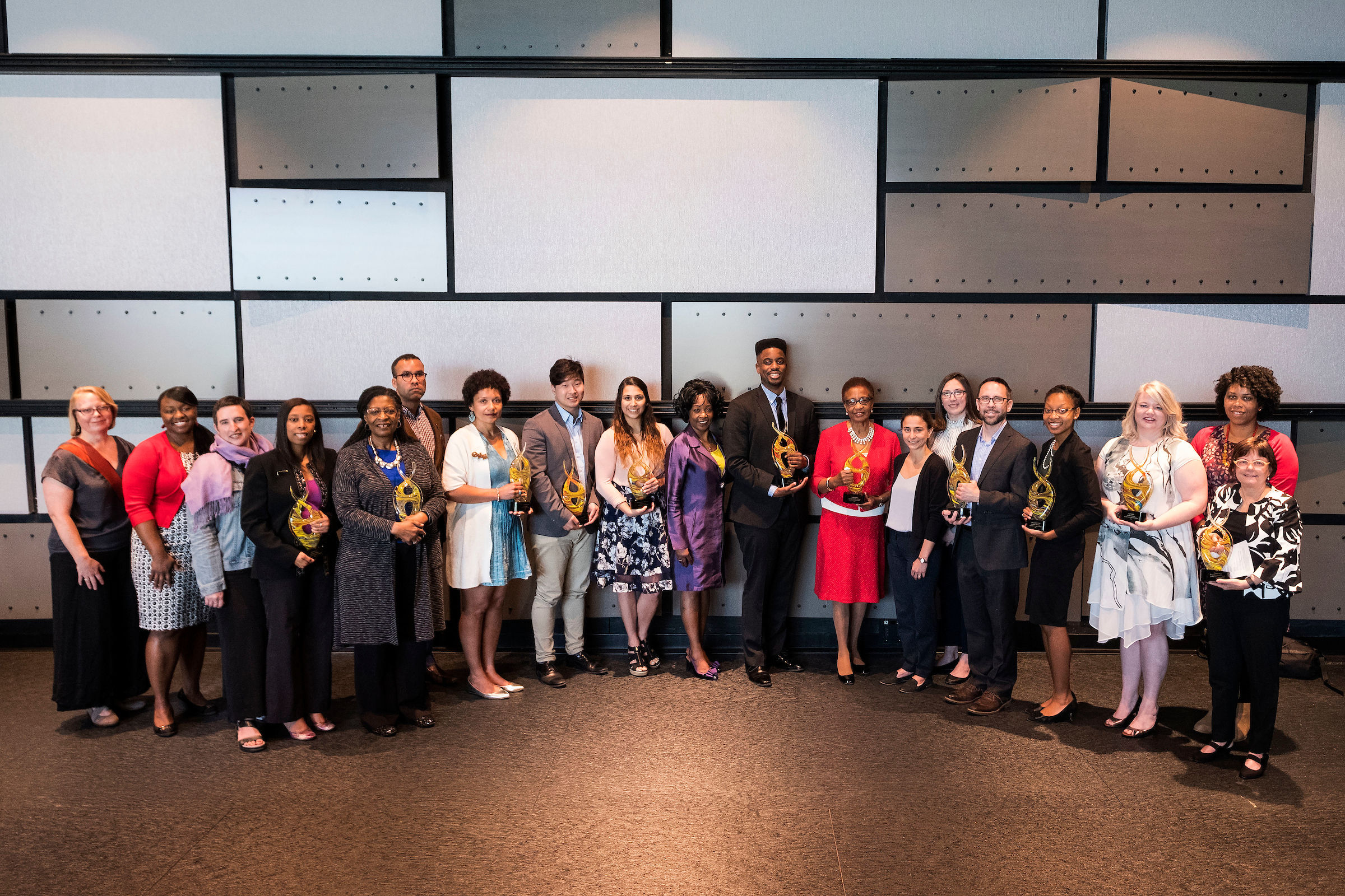Large group of Diversity Award winners pose with their awards in front of a paneled wall.