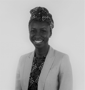 Portrait of Effua Sosoo. Effua is a black woman wearing a patterned headscarf, matching shirt and suit jacket. She is smiling at the camera.
