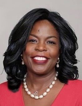 Portrait of Dr. Elmira Mangum. Dr. Mangum is a Black woman with wavy shoulder-length hair. She is wearing a coral blouse, large pearls, a silver necklace and pearl earrings. She is smiling at the camera.