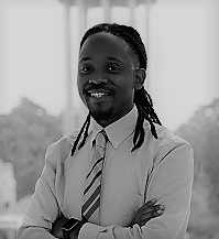 Portrait of Frank Tillman. Frank is a Black man with dreadlocks. He is wearing a light blue collared shirt and striped tie and smiling at the camera.