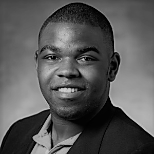 Portrait of Jermaine Bryant. Jermaine is a black man with short black hair. He is wearing a collared shirt and suit jacket and smiling at the camera.