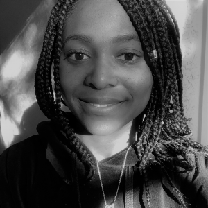 Portrait of Mariel Marshall. Mariel is a Black woman with long braids. She is wearing a black sweatshirt and gold chain and smiling at the camera.