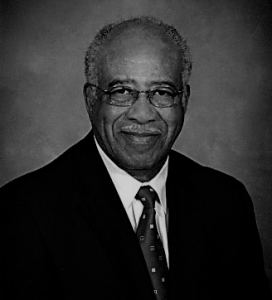 Portrait of Senator Howard Lee. Senator Lee is a black man with gray hair. He is wearing glasses and a suit with a polka dot tie and smiling at the camera.