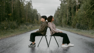 Two people sitting back-to-back in the middle of a road